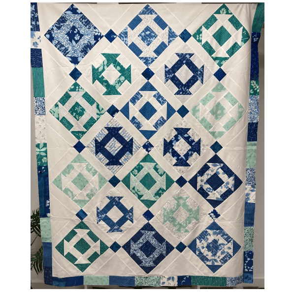 A handmade quilt with a geometric diamond pattern in shades of navy, teal, and mint green on an off-white background, featuring a decorative border.