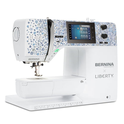 A white Bernina x Liberty sewing machine with a blue and white floral patterned upper housing, a digital display screen, and a flatbed base, shown on a solid white background.