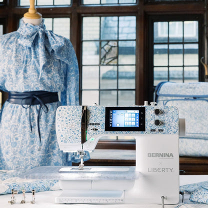 A BERNINA LIBERTY sewing machine in white with a blue floral pattern, displayed in a room with a matching blue floral dress on a mannequin and a blue floral quilt in the background.