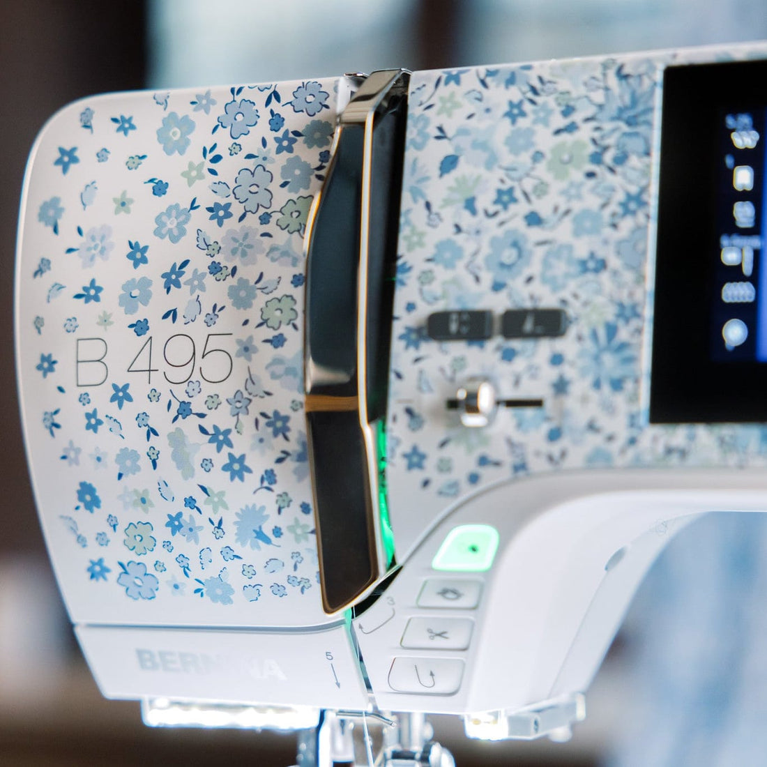 Close-up of a BERNINA sewing machine with a blue and white floral patterned finish, featuring a digital display screen and control buttons.