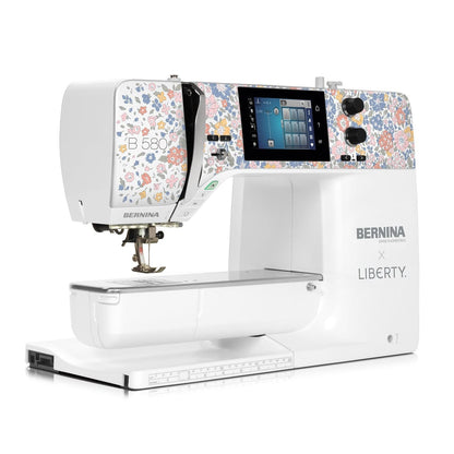 A BERNINA Liberty sewing machine in white, featuring a colorful floral pattern on the upper sides and a digital display screen, shown on a clean white background.