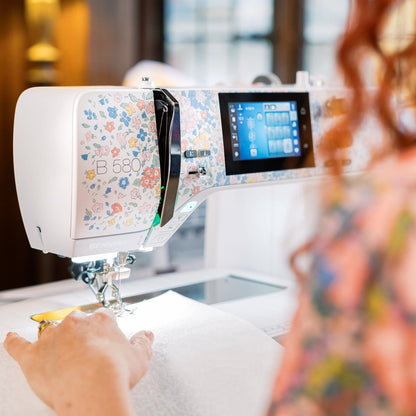 Person using a sewing machine with a digital display in a well-lit room.