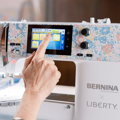 Sewing machine with Liberty fabric design and a hand interacting with the touchscreen.