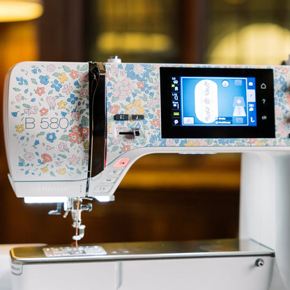 A BERNINA B 580 Liberty sewing machine with a white body and a colorful floral pattern on the upper housing, featuring a digital screen and control knobs.