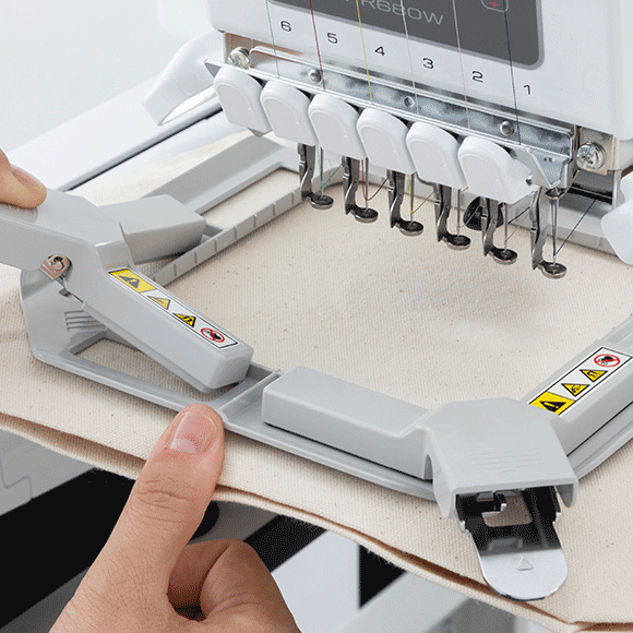 Embroidery machine with a person adjusting a piece of fabric.