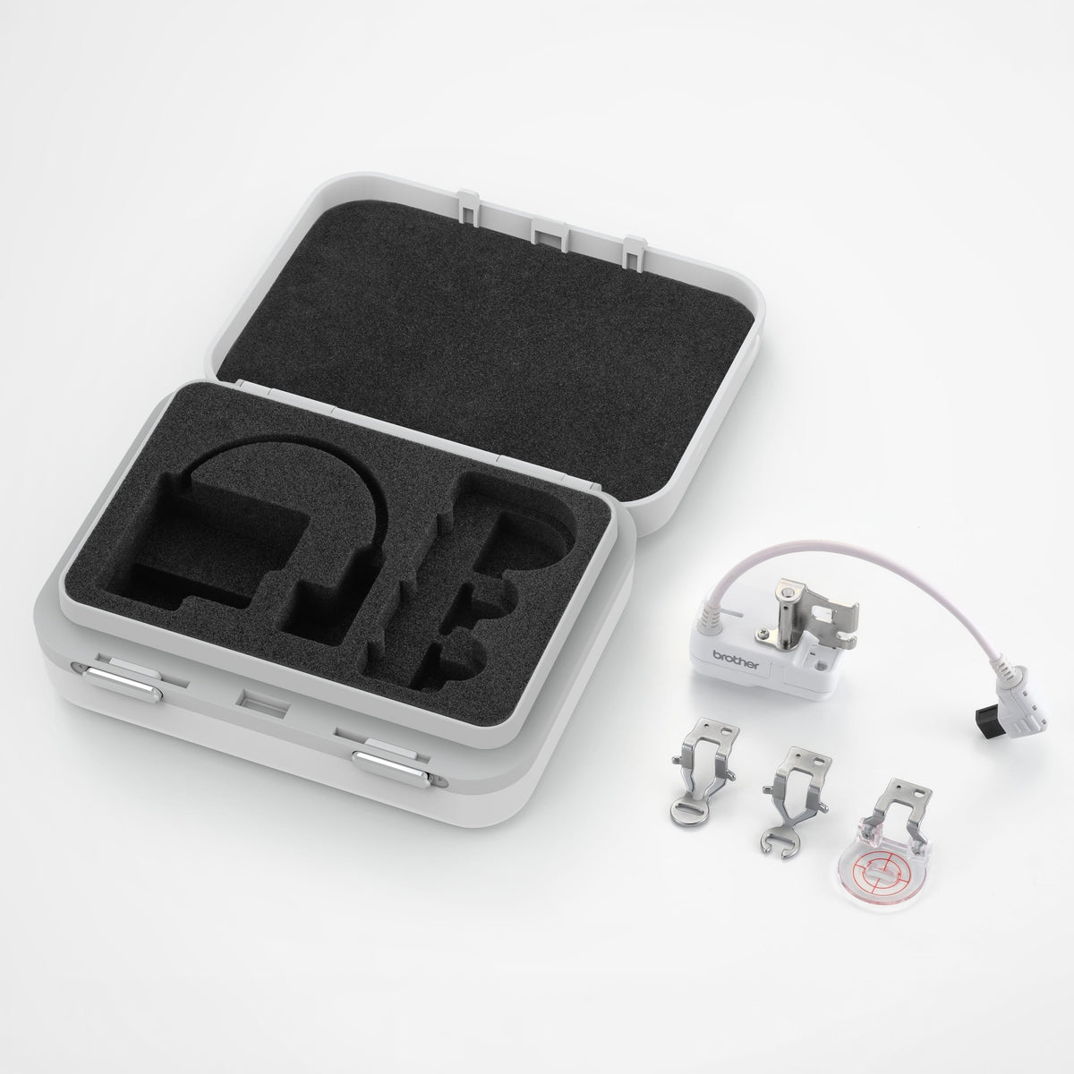 An open light gray hard carrying case with black foam inserts, shown on a white background alongside a small white electronic module with a cable, three metal clips, and a round clear accessory.