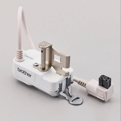 A Brother sewing machine accessory with a white plastic body, silver metal press foot, and a light pink cord, shown on a neutral light gray background.