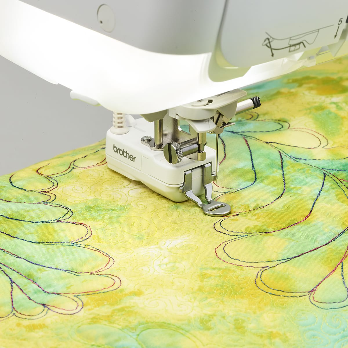 A close-up of a Brother sewing machine stitching a light green and yellow quilted fabric with decorative curved lines.