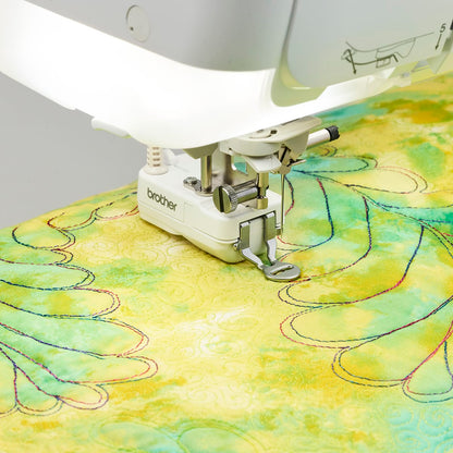 A close-up of a Brother sewing machine stitching a light green and yellow quilted fabric with decorative curved lines.