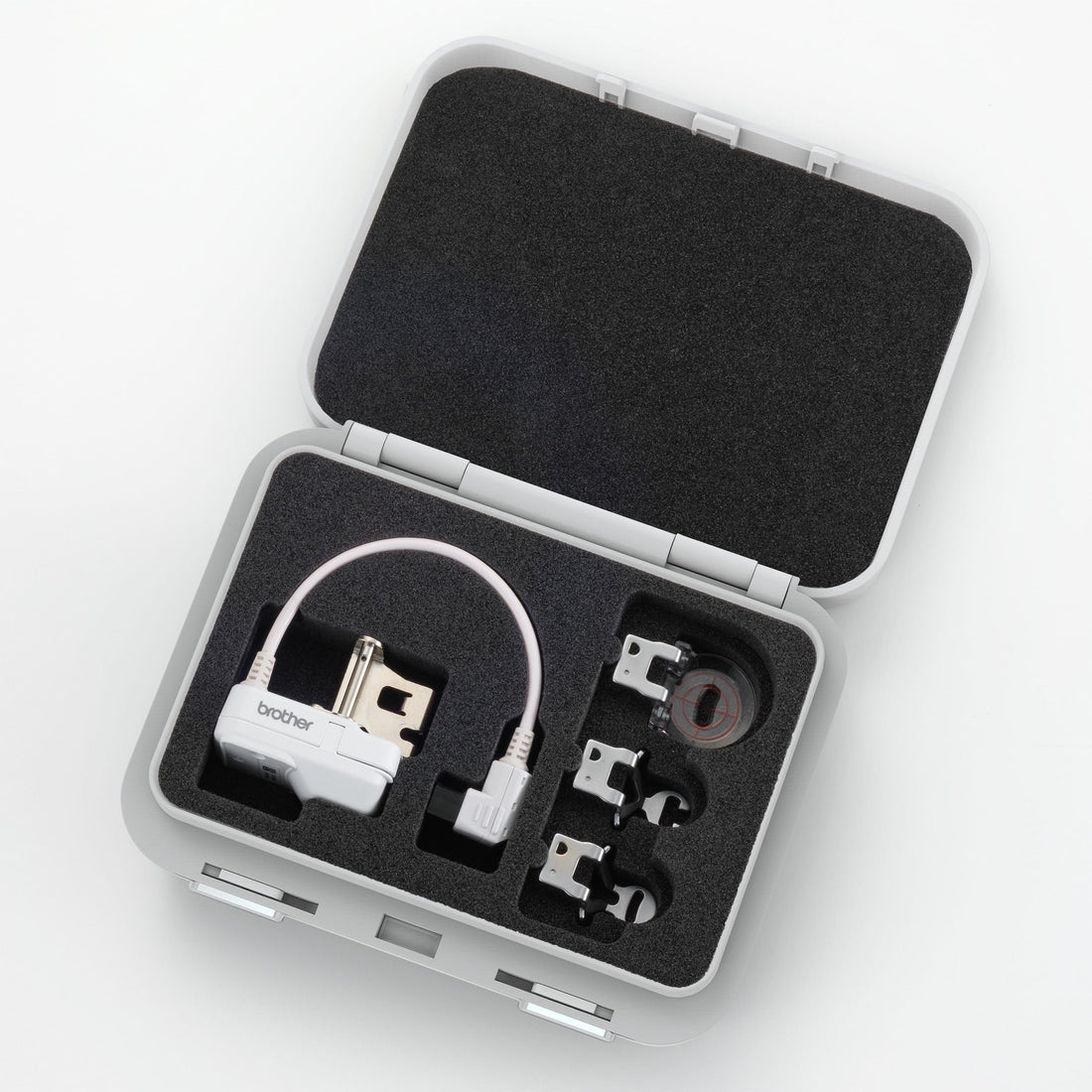 An open gray hard carrying case with black foam insert, containing a white electronic device with a cable and several small accessories, photographed on a clean white background.