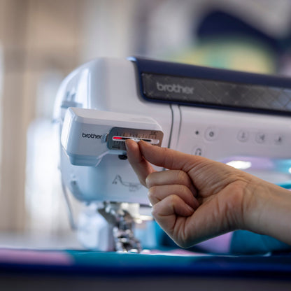 A close-up of a Brother sewing machine with a person's hand adjusting a dial on the front panel.