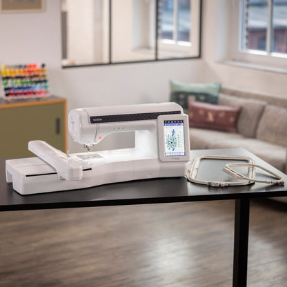A white sewing machine with an attached embroidery thread spool holder and a small display screen, placed on a black table in a modern living room setting.