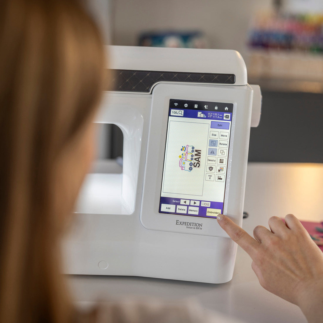 A close-up of a person's hand touching the touchscreen interface of a white Eversoft sewing machine in a bright, softly blurred craft room.