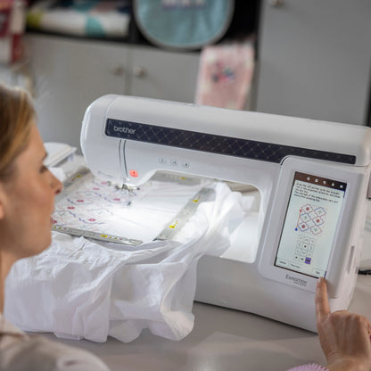 A woman uses a Brother embroidery machine to create a white embroidered garment in a bright, modern craft room.