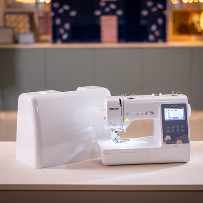 A white Brother sewing machine with an attached large white fabric storage bag sits on a light-colored table in a softly blurred indoor setting.