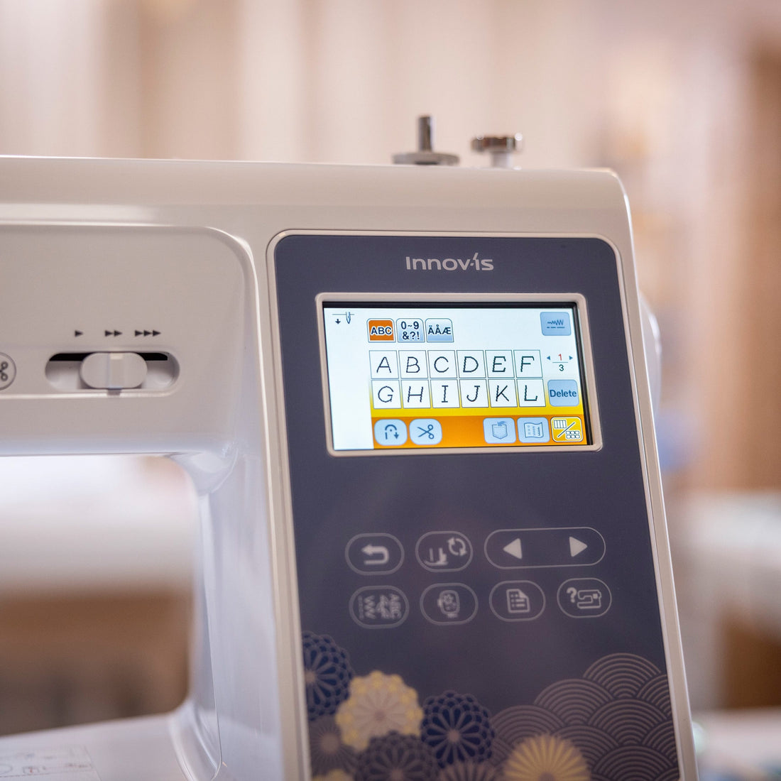 A close-up of a white Innovis sewing machine with a digital touchscreen interface and decorative floral patterns on the control panel, set against a softly blurred indoor background.