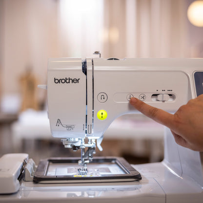 A close-up of a Brother Innov-is sewing machine with a person's finger pressing a button on the control panel, set against a softly blurred indoor background.