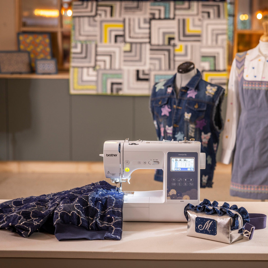 A sewing machine on a table with navy patterned fabric, a small matching bag, and a dress displayed in a styled interior setting.
