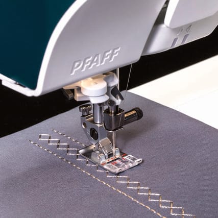 Close-up of a PFAFF sewing machine pressing fabric with a zigzag stitch pattern, showing the press foot and needle area.