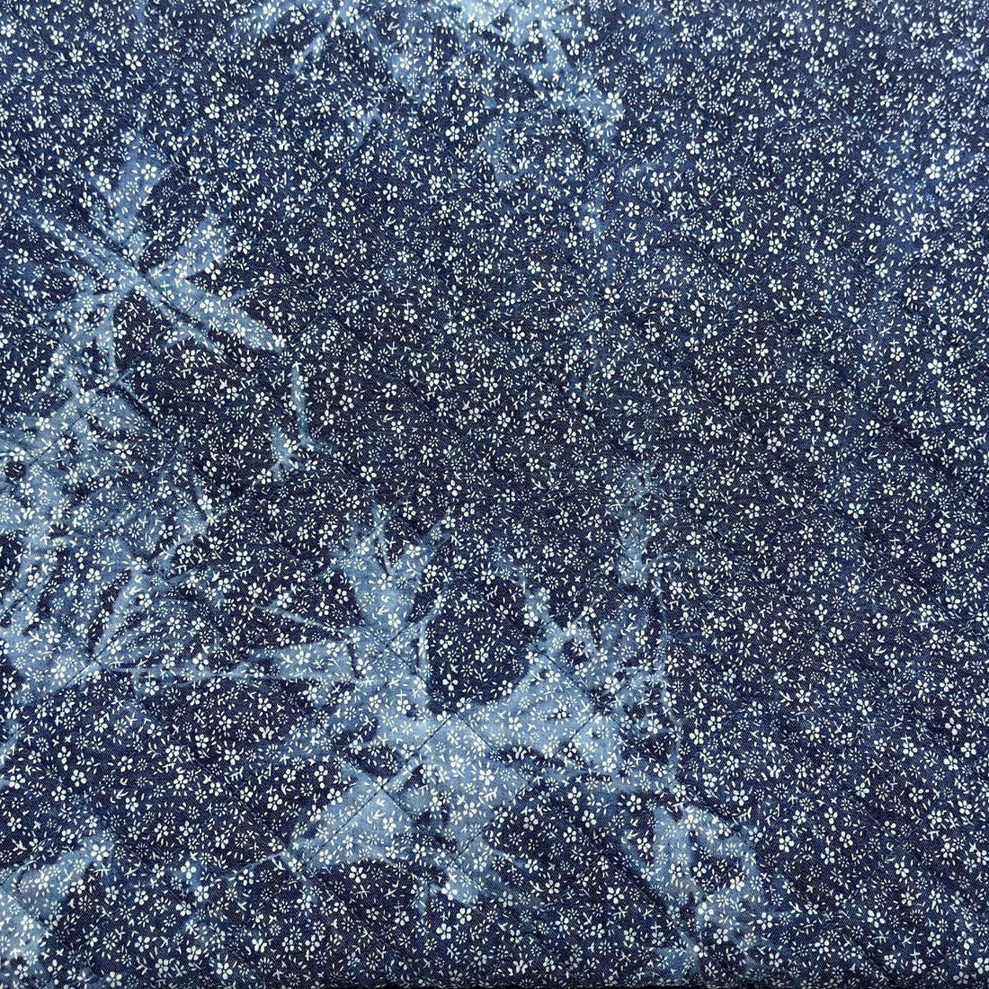 A close-up of a dark navy blue fabric with dense white floral or snowflake-like printed motifs and a subtle icy sheen.